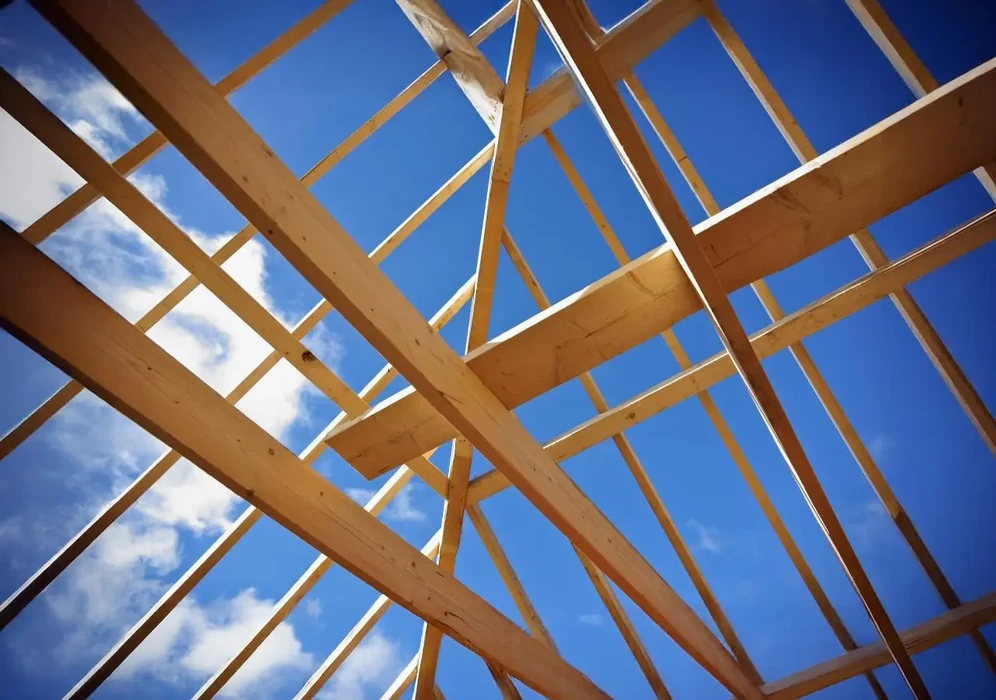 Chantier de construction extérieur avec charpente en bois massif en cours d'assemblage sous ciel bleu nuageux