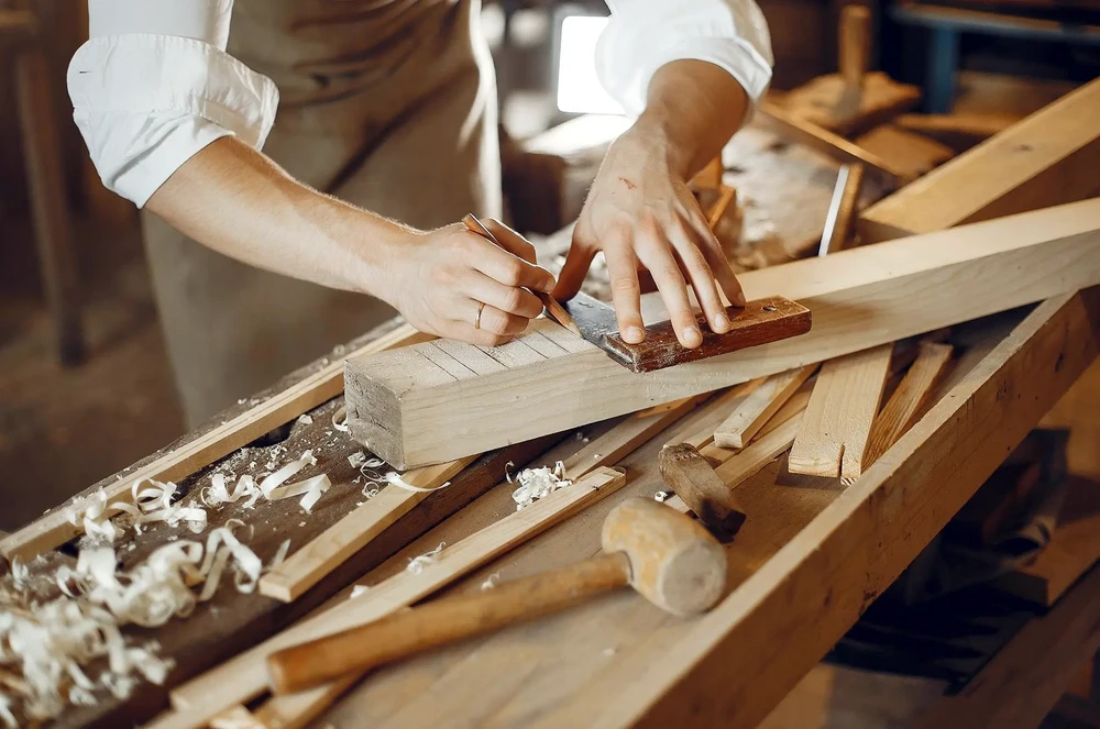 Atelier de menuiserie avec quatre artisans collaborant autour d'un &eacute;tabli en bois massif
