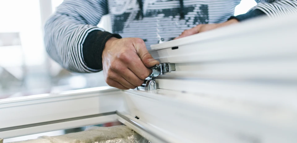 Artisan menuisier travaillant sur une fenêtre en bois, utilisant un rabot manuel pour ajuster le châssis